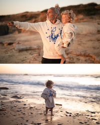 Mann mit Kind auf dem Arm am Strand Ankerherz Hoodie EUROPA ONE LOVE Ivory Garment Dye, blauer Siebdruck Europa auf Zeus-Stier mit zwölf Sternen von Dani Garreton, Unisex Frontansicht